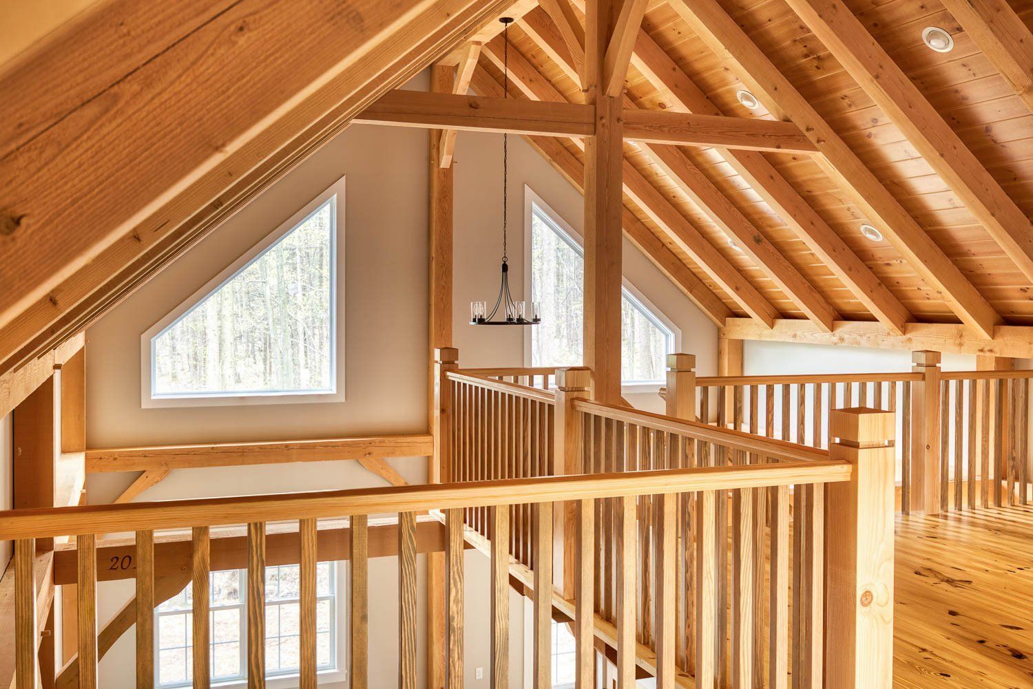 Wooden interior with a balcony, triangular windows, and exposed beams.
