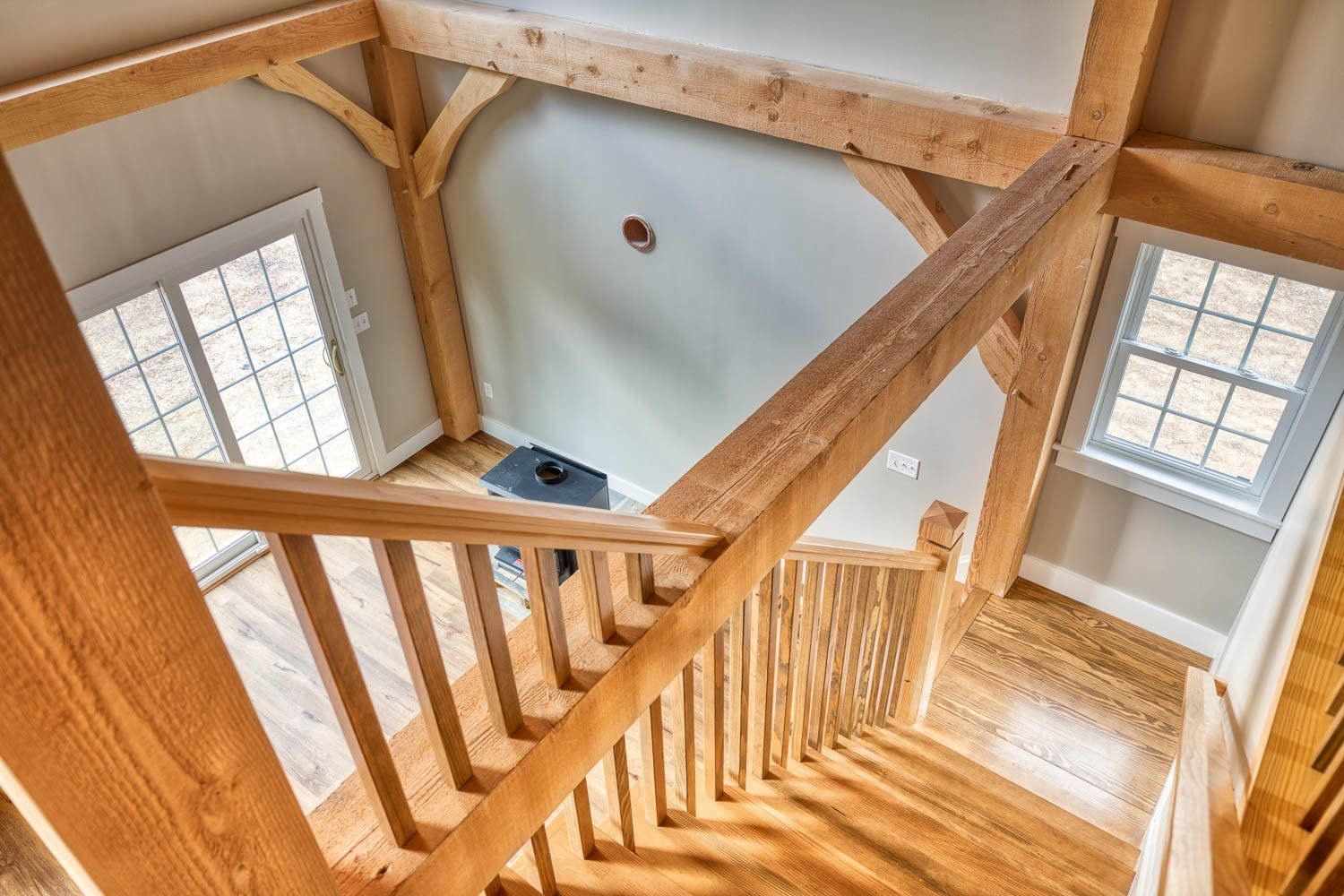 Wooden staircase with exposed beams, viewed from above. Light wood with two windows.