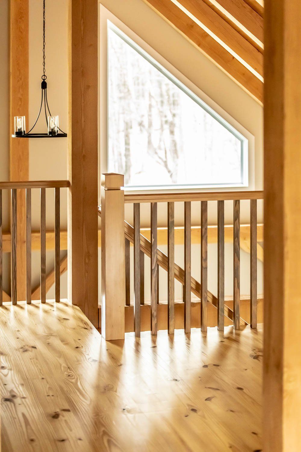 Wooden railing and floor inside a light-filled room with a triangular window and beams overhead.