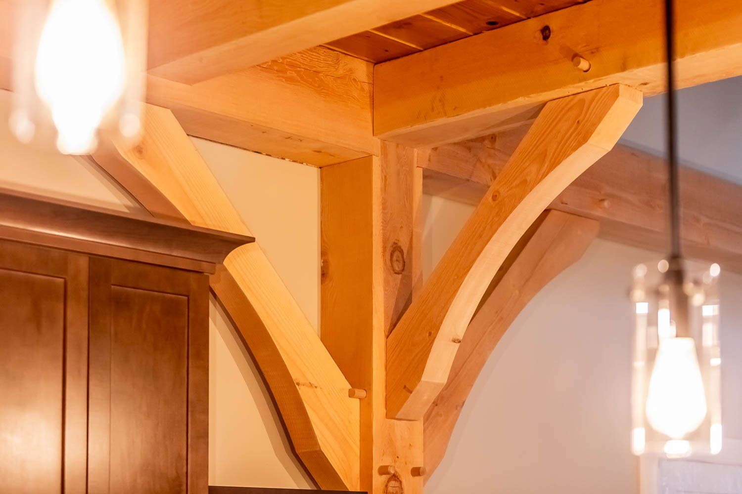 Wooden support beams in a room, featuring curved braces and warm lighting.