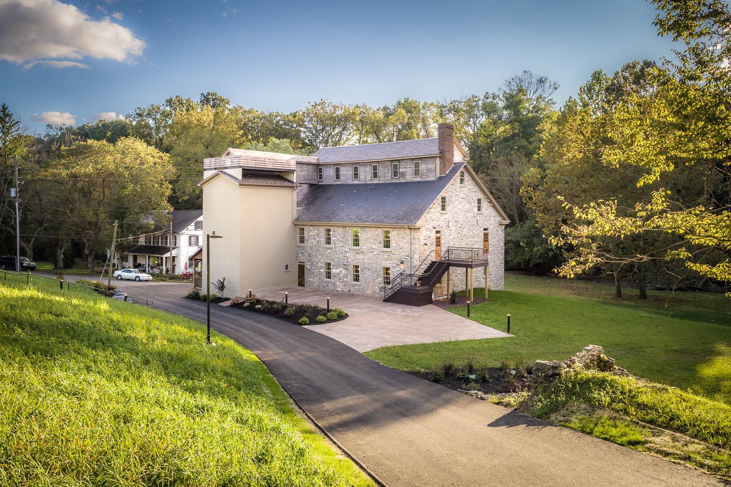 Stone building with tall tower, surrounded by trees and a paved driveway.