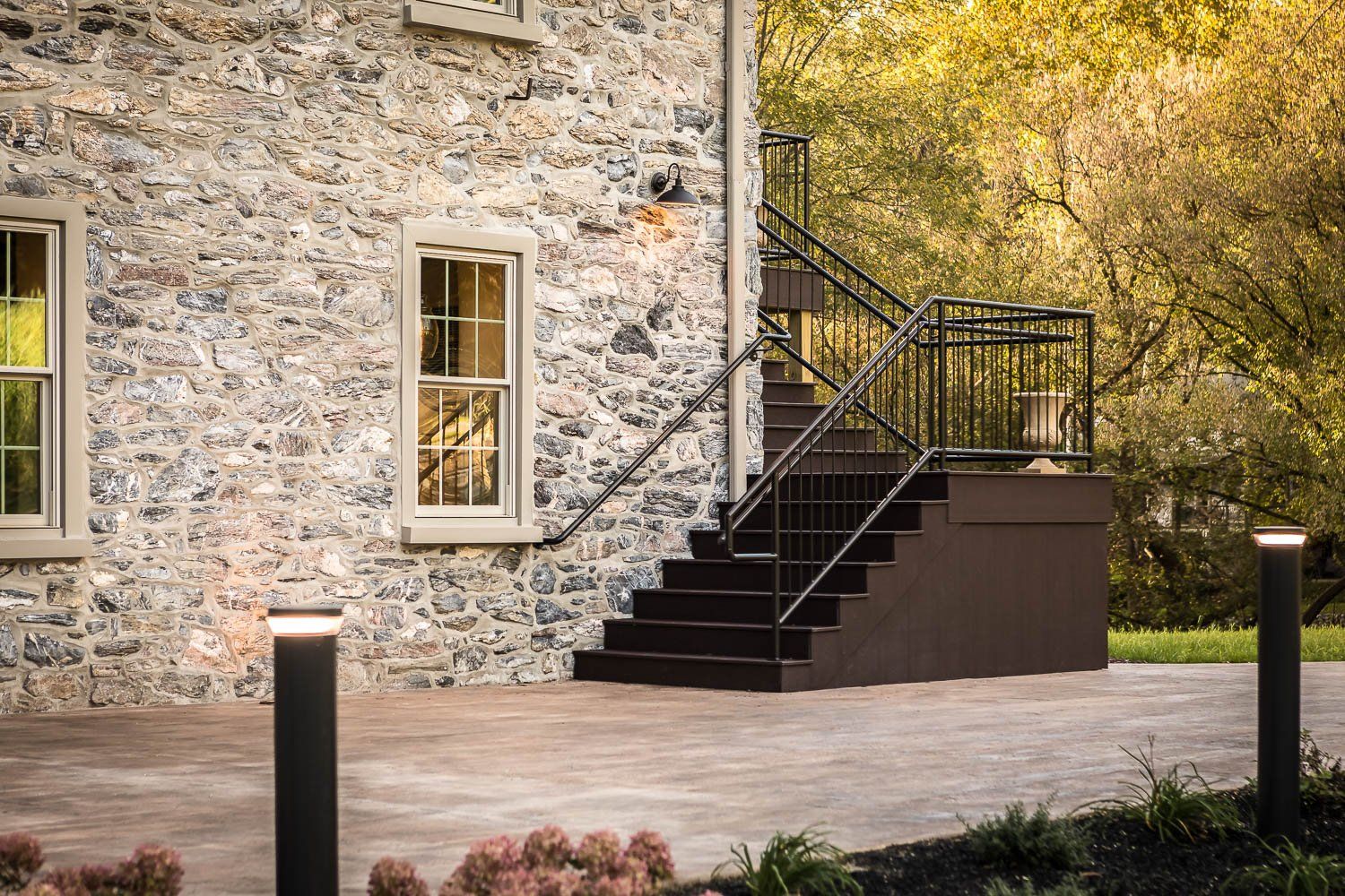 Stone building with stairs and outdoor lighting. Brown stairs and pathway. Green trees in background.