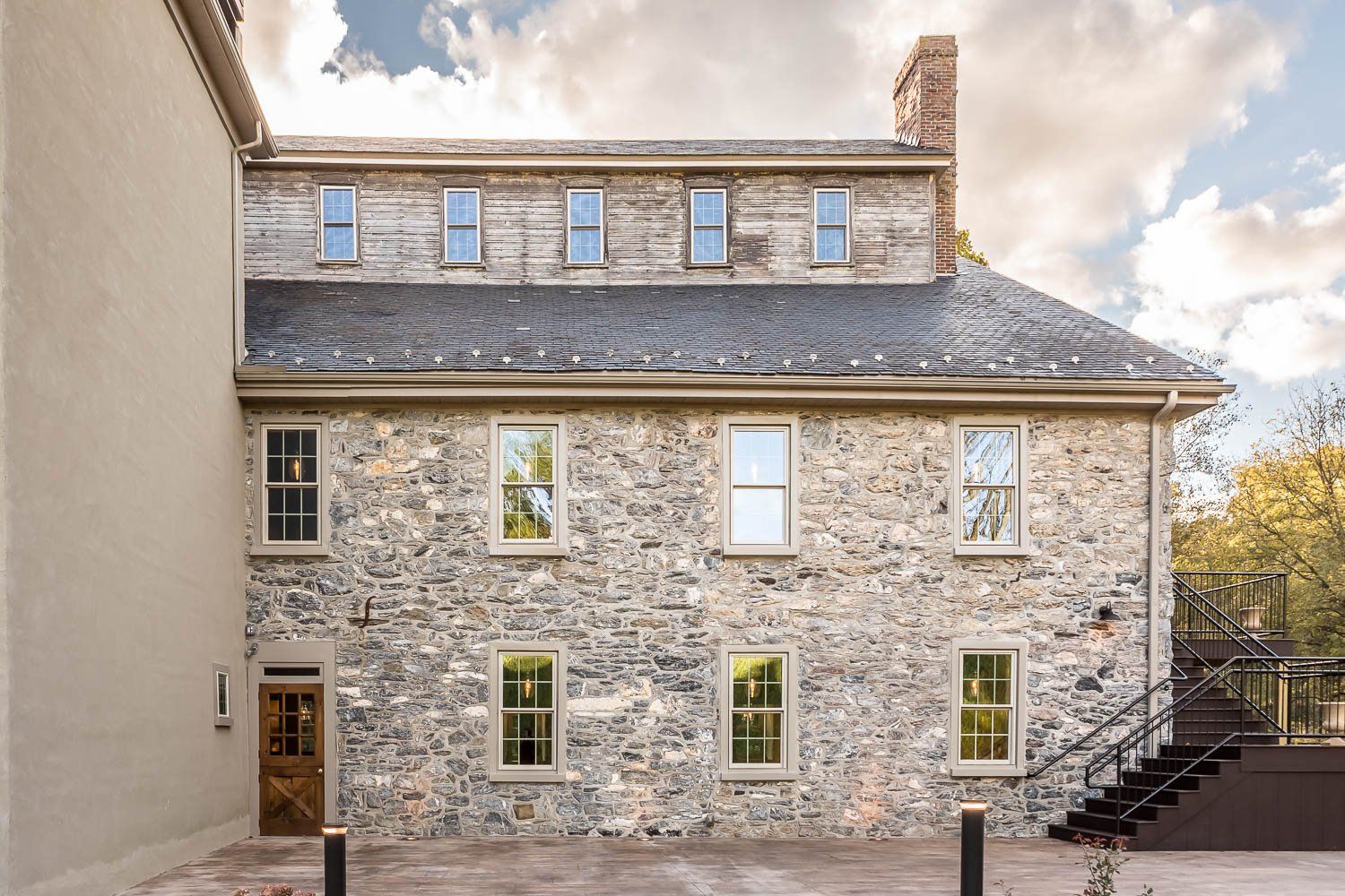 Stone building with multiple windows under a slate roof; brown door, black stairs.