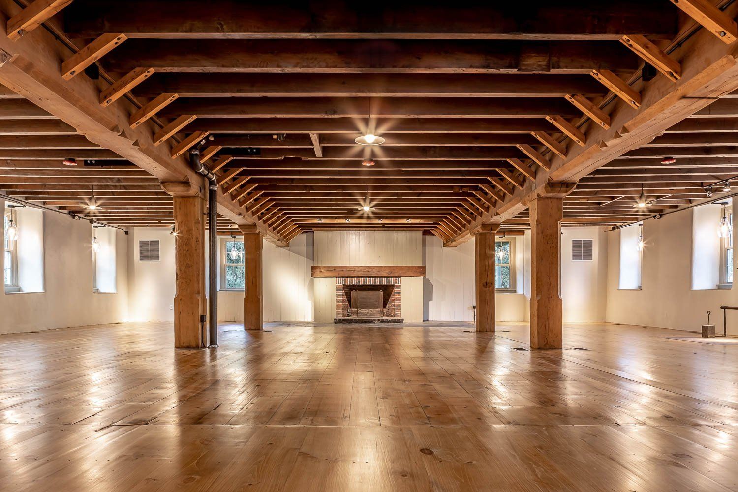 Wooden-beamed interior with hardwood floor, fireplace, and supporting columns.