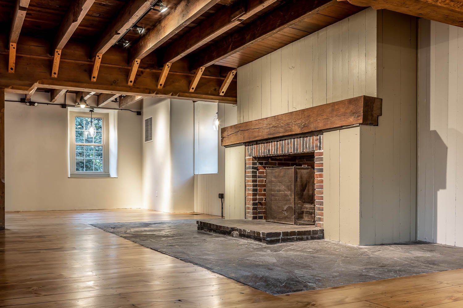 Empty room with fireplace, wooden beams, hardwood floor, and a rug.