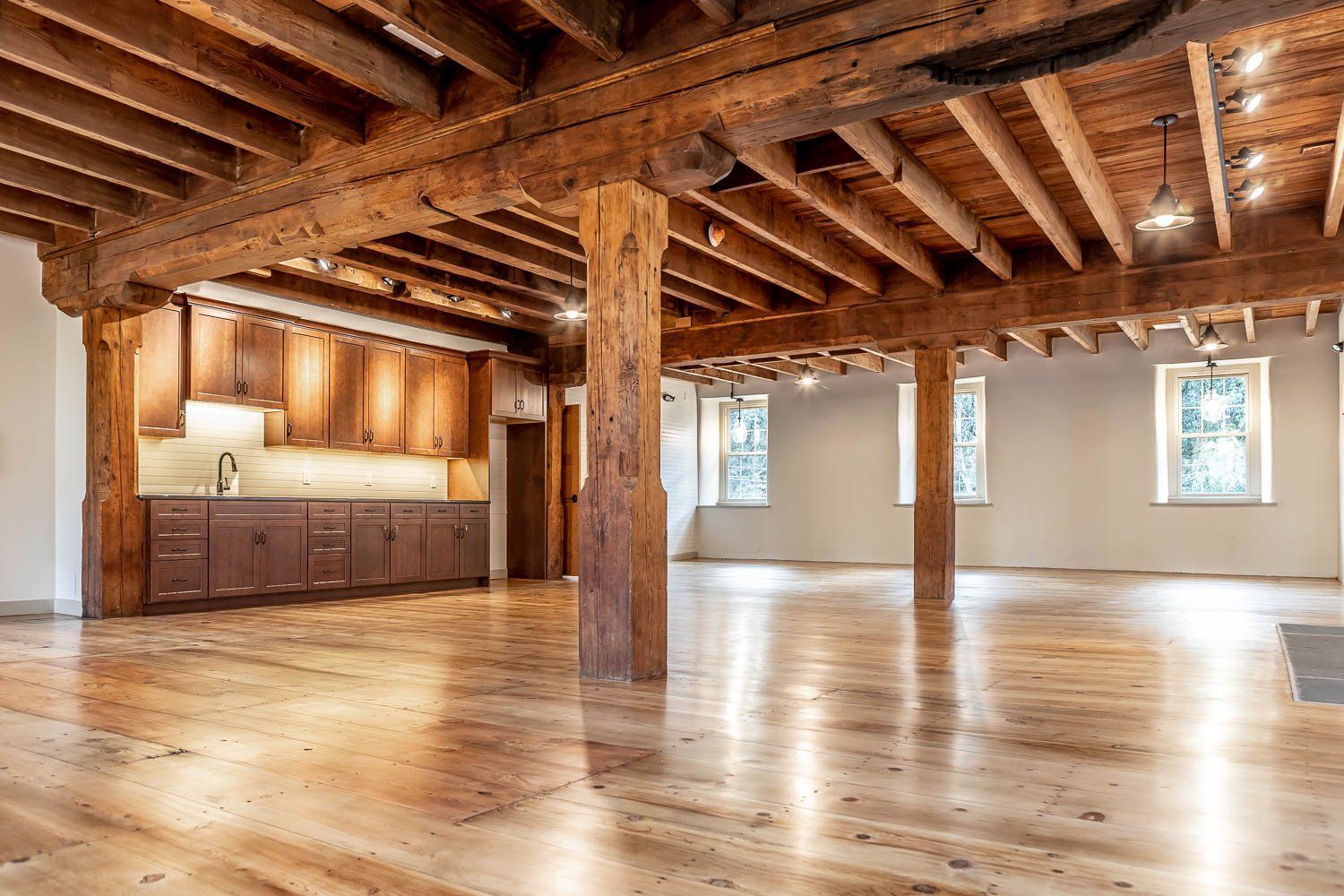 Spacious room with exposed wooden beams, hardwood floors, and a small kitchen area.