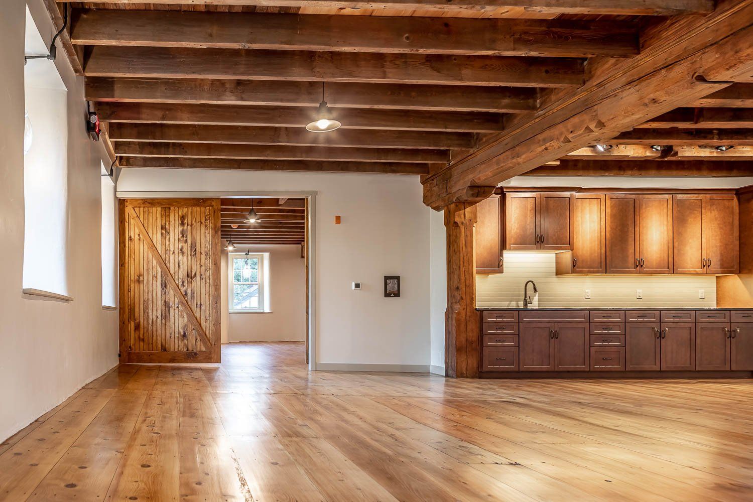 Spacious interior with wood floors, exposed beams, a rustic sliding door, and a built-in kitchen.
