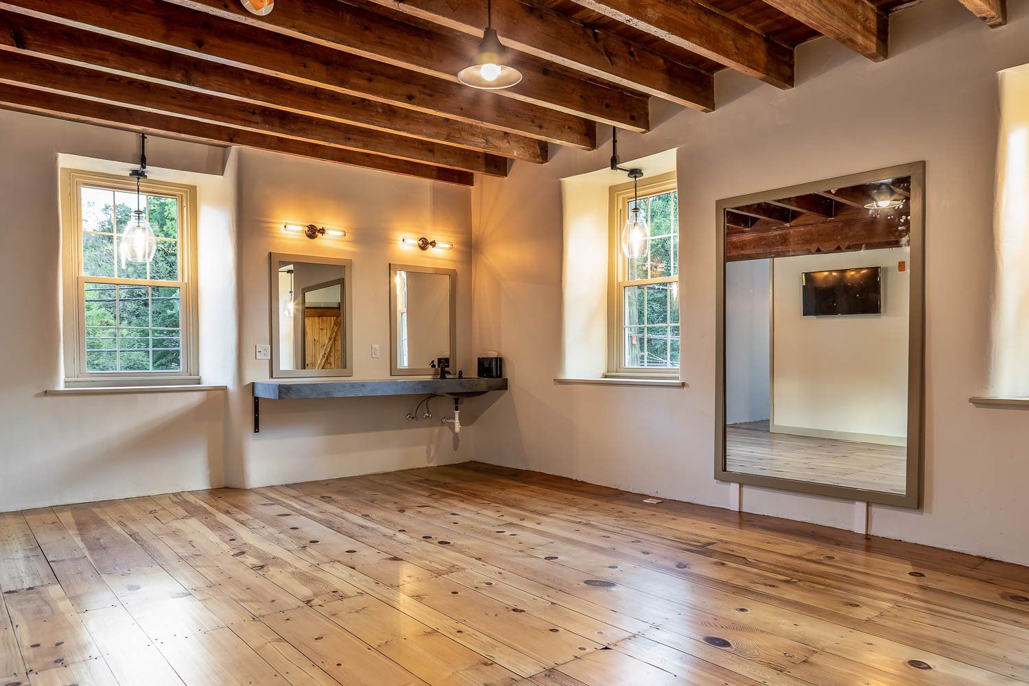Empty room with wood floors, exposed beams, and large mirrors. Windows let in natural light.