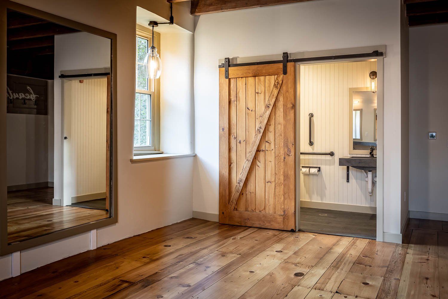 Wooden floor room with open wooden sliding door to bathroom. Large mirror on left.