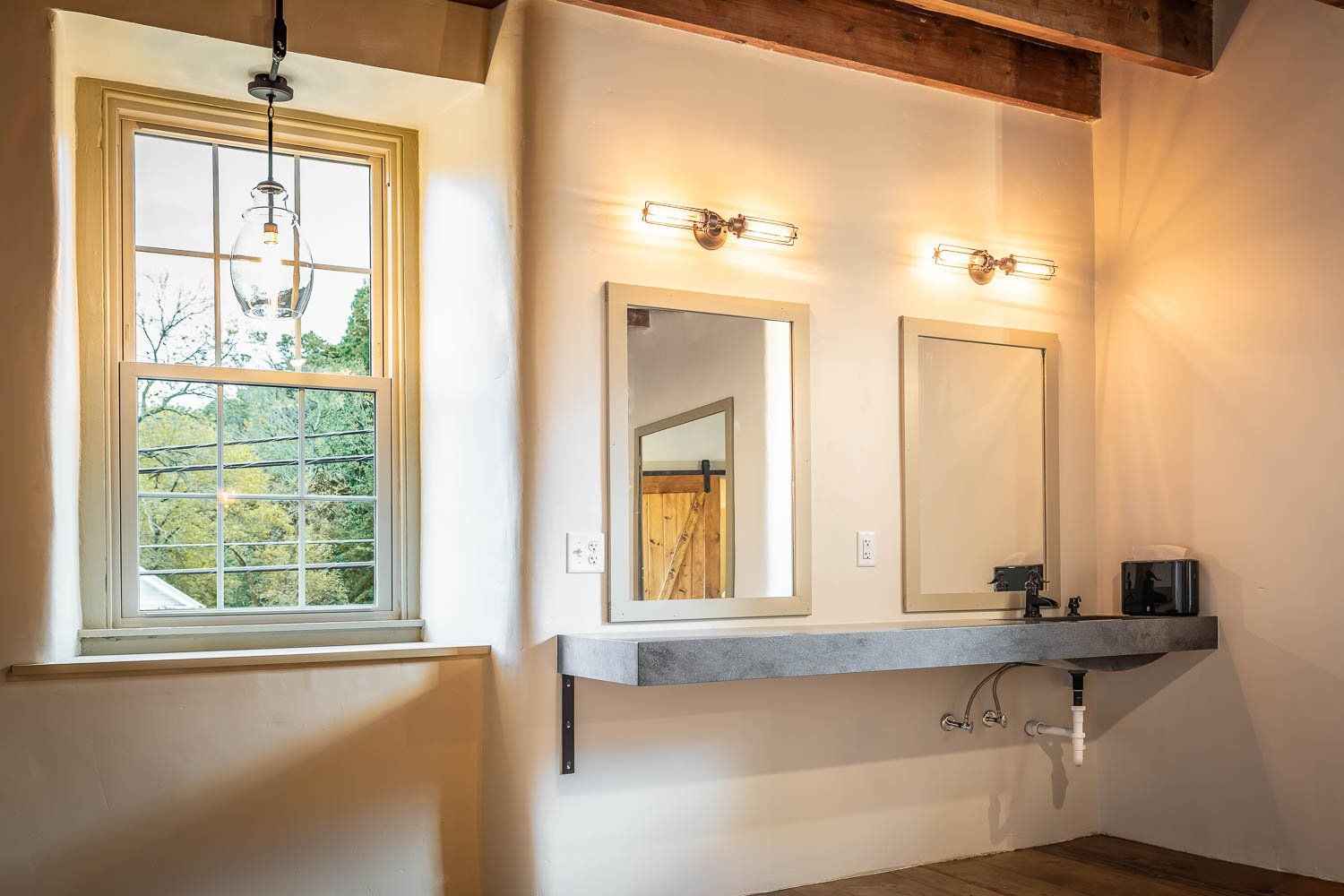 Bathroom with concrete counter, two mirrors, and a window overlooking trees.