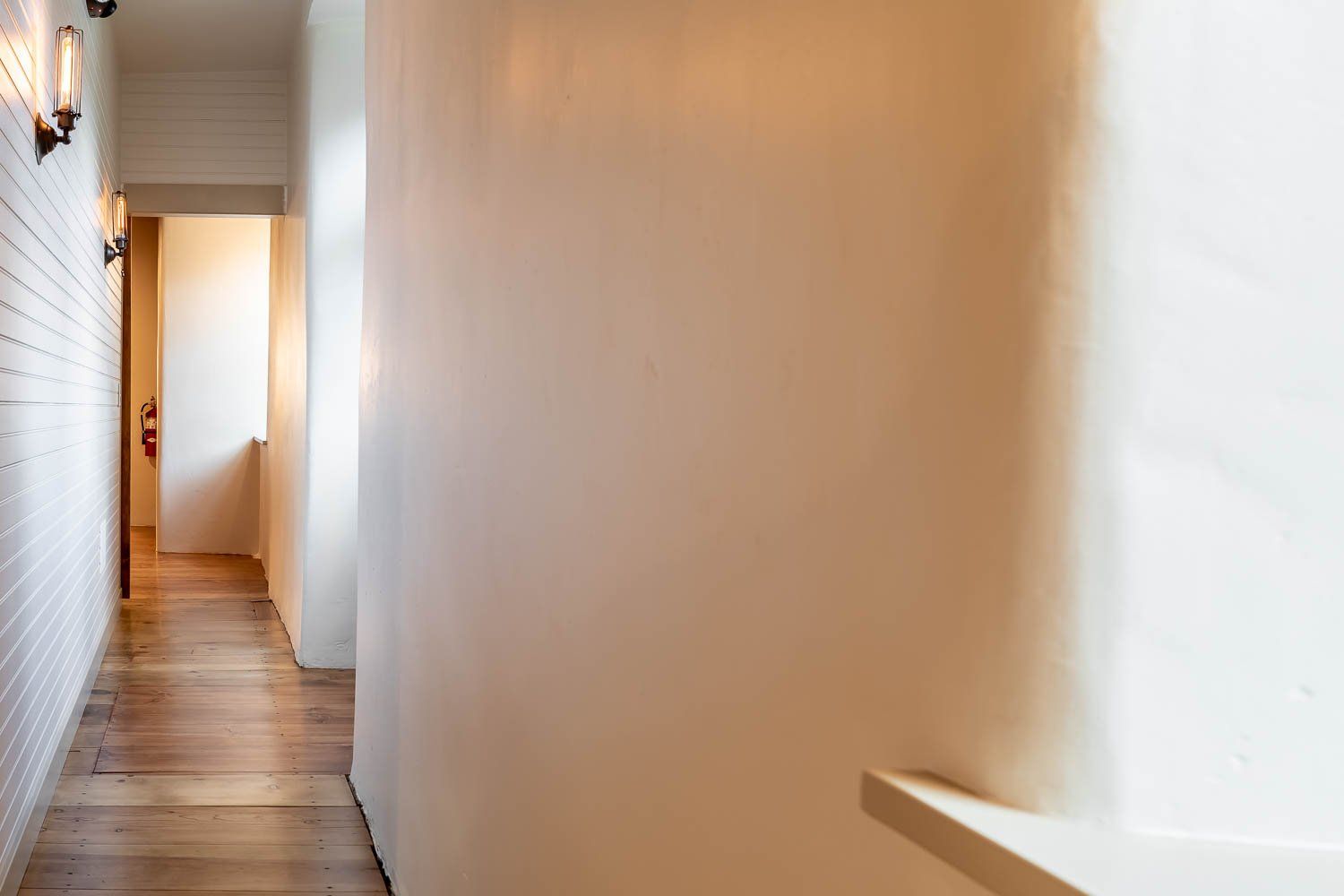 Long hallway with wood floor and white walls. Light fixtures on the left.