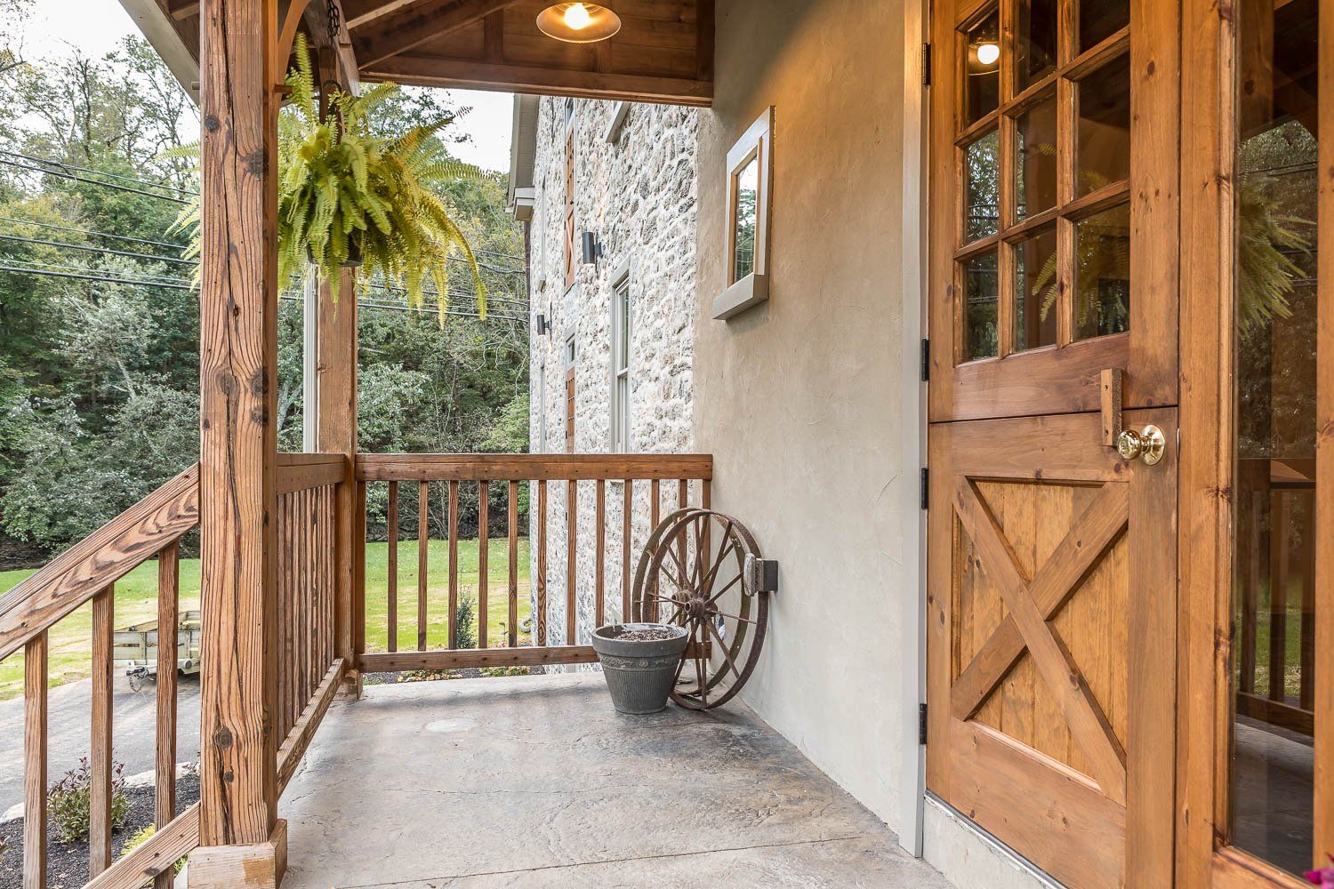Wooden porch with a rustic door, stone wall, and a wagon wheel.