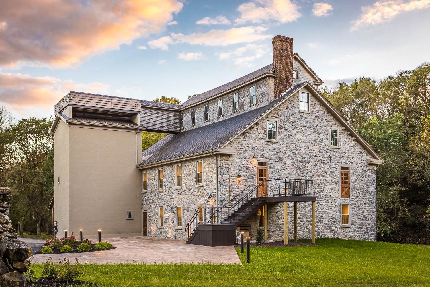 Stone building with a connecting walkway, chimney, and manicured lawn. Evening sky above.