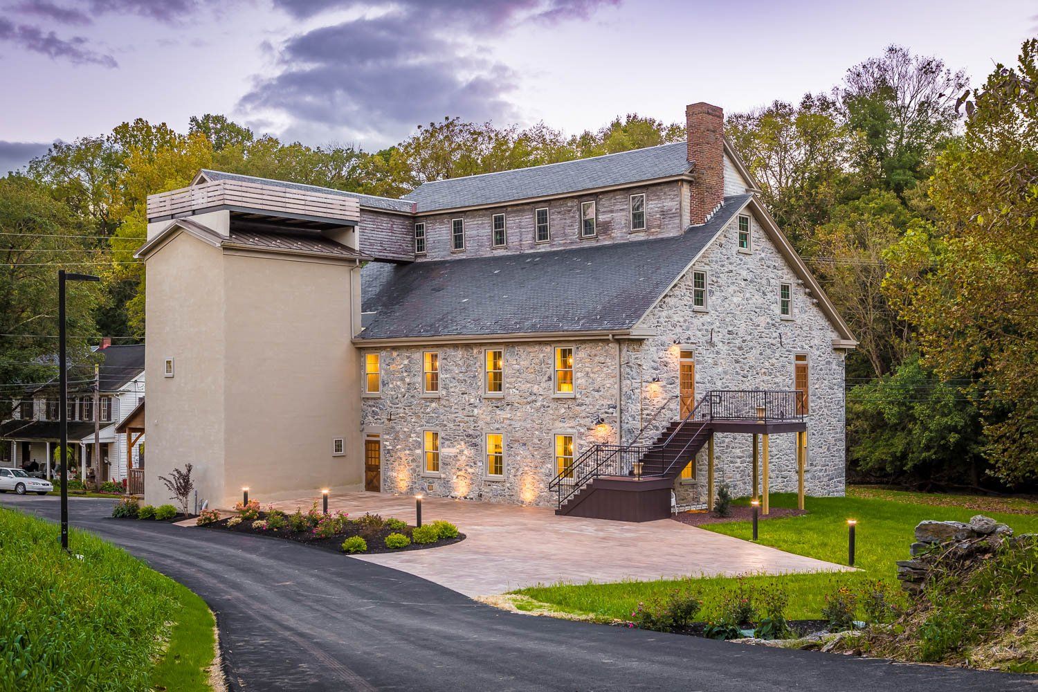 Stone building with attached tower, parking area, and grassy lawn, trees in background.