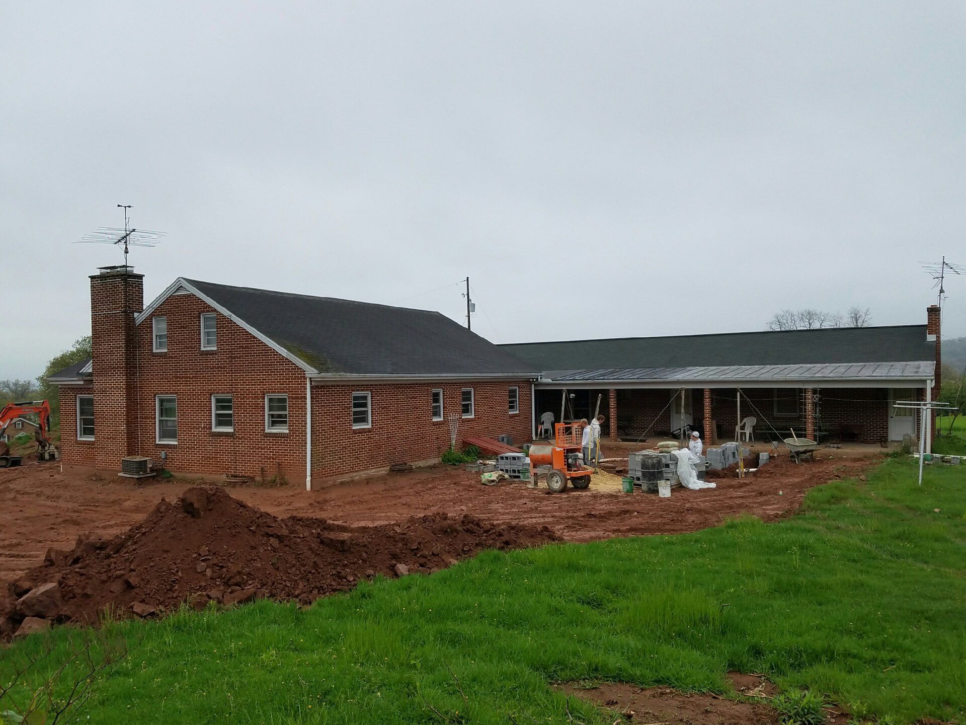 Brick house under construction with exposed patio area and dirt lot.