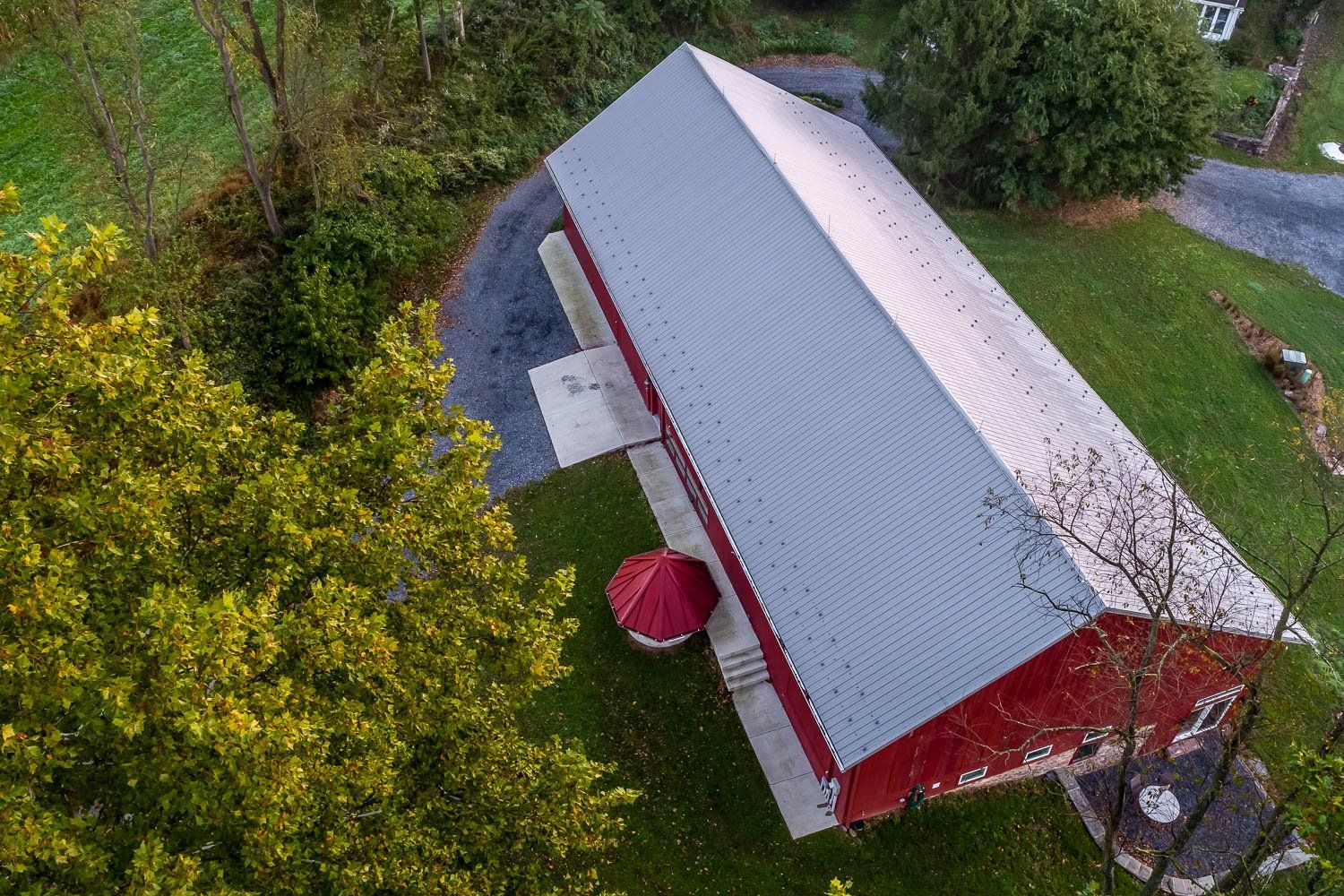 Aerial view of a red barn with a gray metal roof, surrounded by green grass and trees.