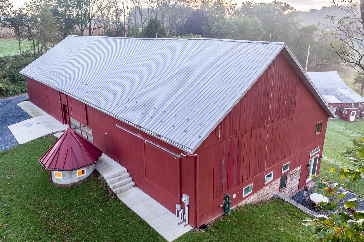 Red barn with silver roof on green grass, round red structure attached.