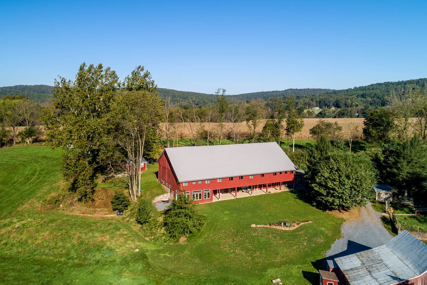 Red barn with a gray roof on a green hill, trees and field in the background.