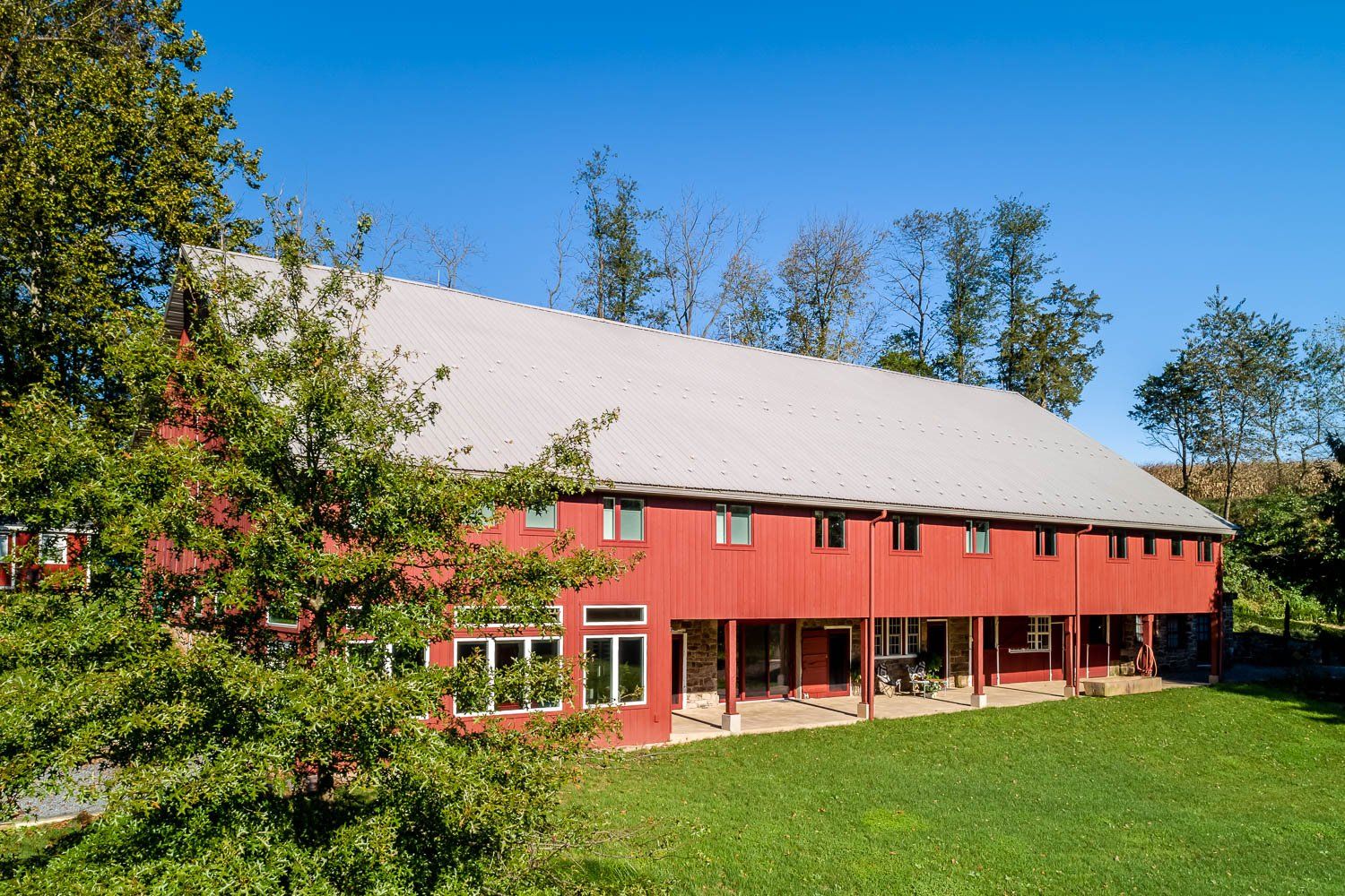 Red barn with a long, silver roof on a green lawn under a blue sky.
