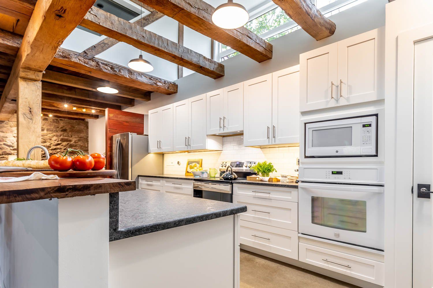 Kitchen with white cabinets, dark countertops, exposed wooden beams, and brick wall.