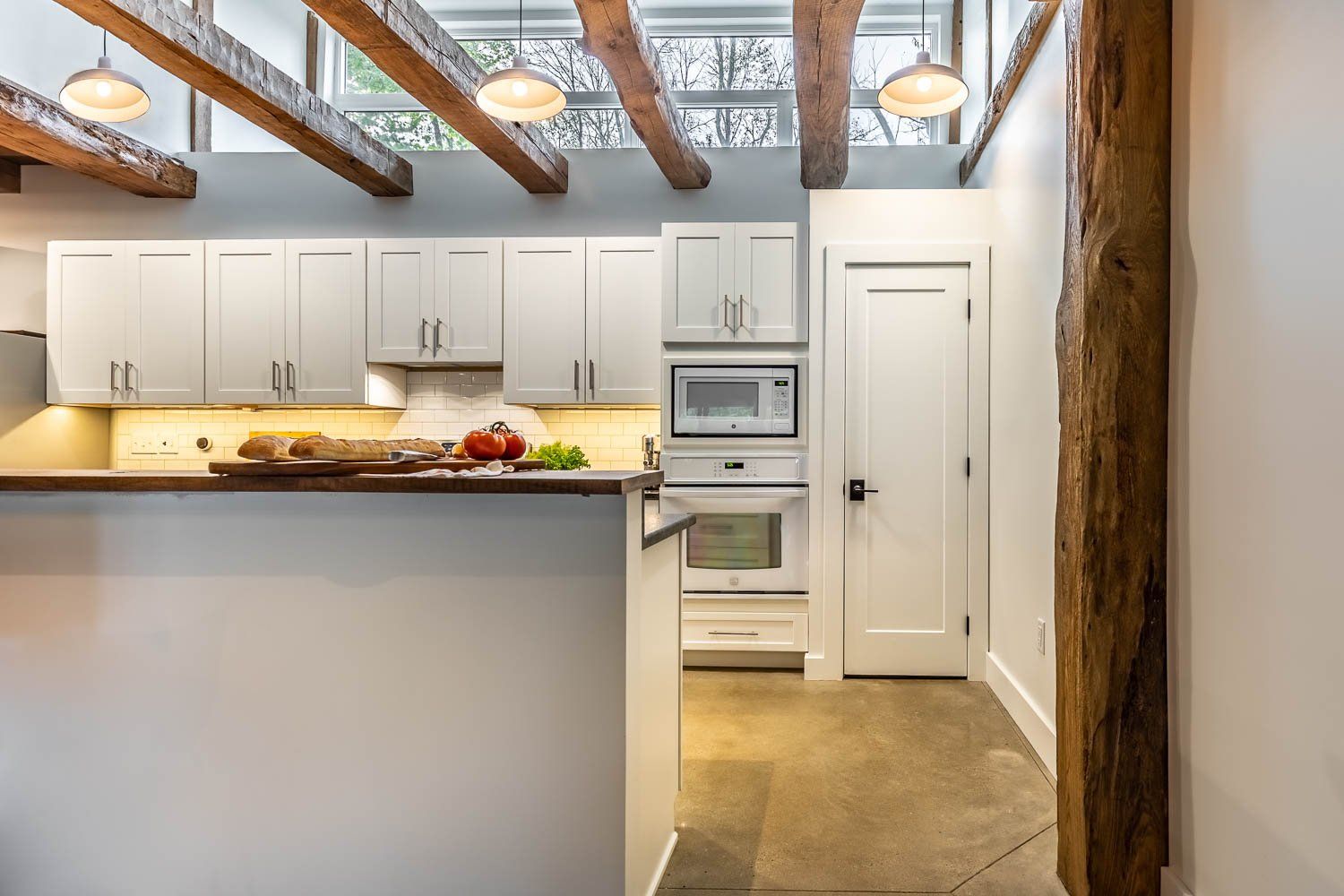 Modern white kitchen with wooden beams and a concrete floor.