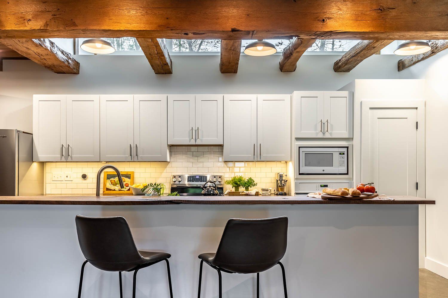Modern kitchen with white cabinets, wood beams, and a breakfast bar with two black chairs.