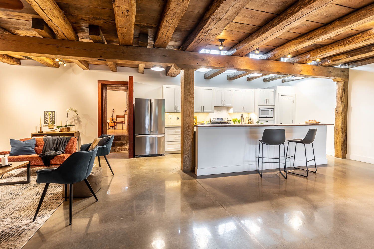Open-concept living space with exposed wooden beams, polished concrete floor, kitchen with a breakfast bar, and seating area.