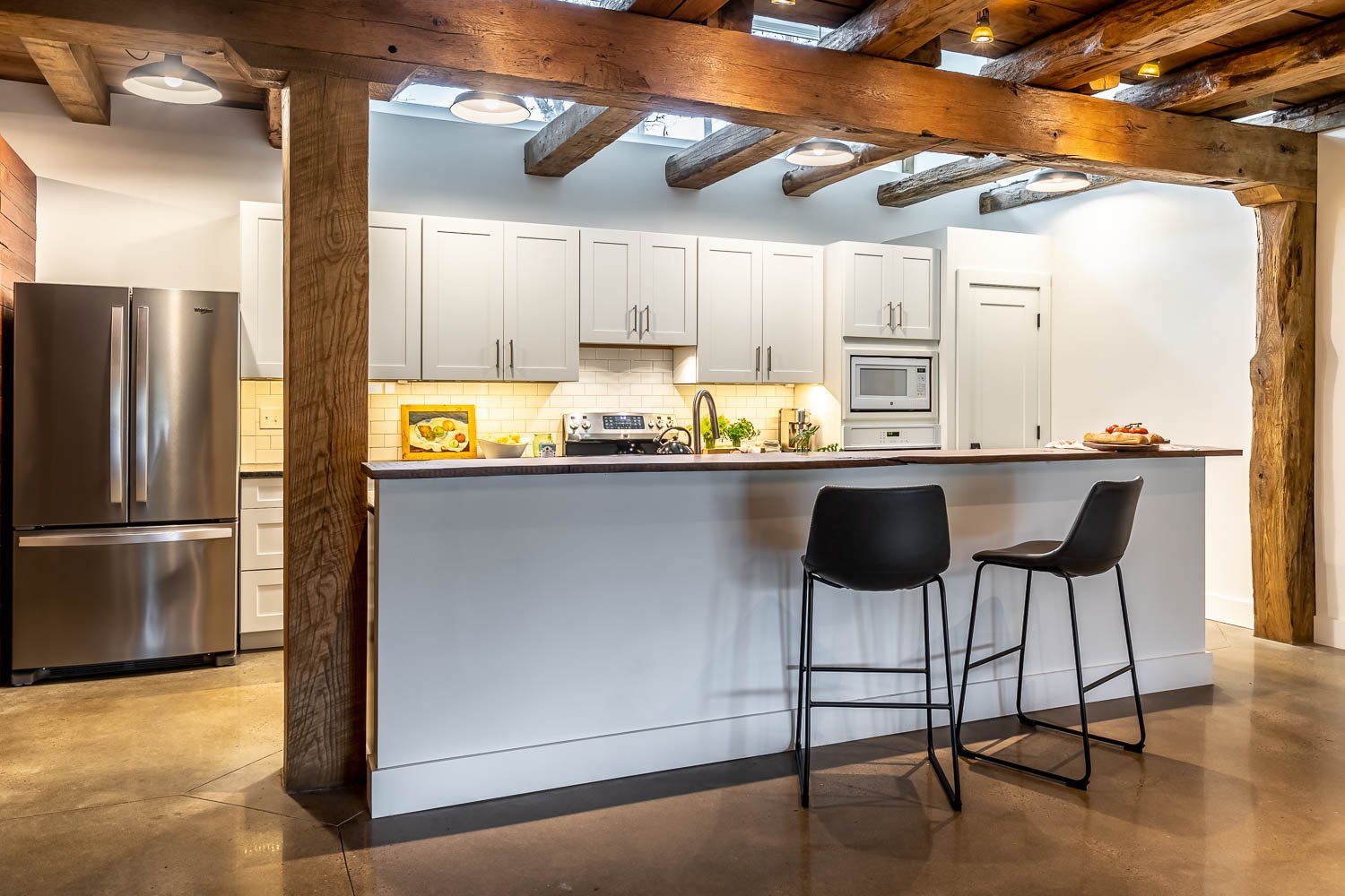 Modern kitchen with stainless steel appliances, white cabinets, and a breakfast bar with two stools.