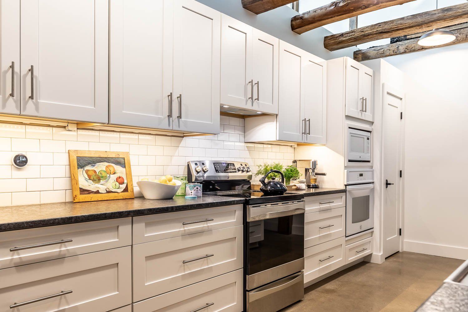 White kitchen with cabinets, stainless steel appliances, and exposed wooden beams.
