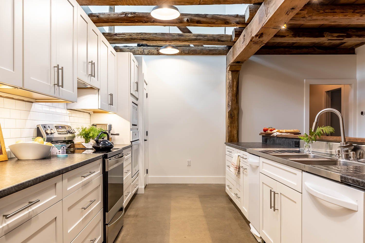 Modern kitchen with white cabinets, dark countertops, and exposed wooden beams.