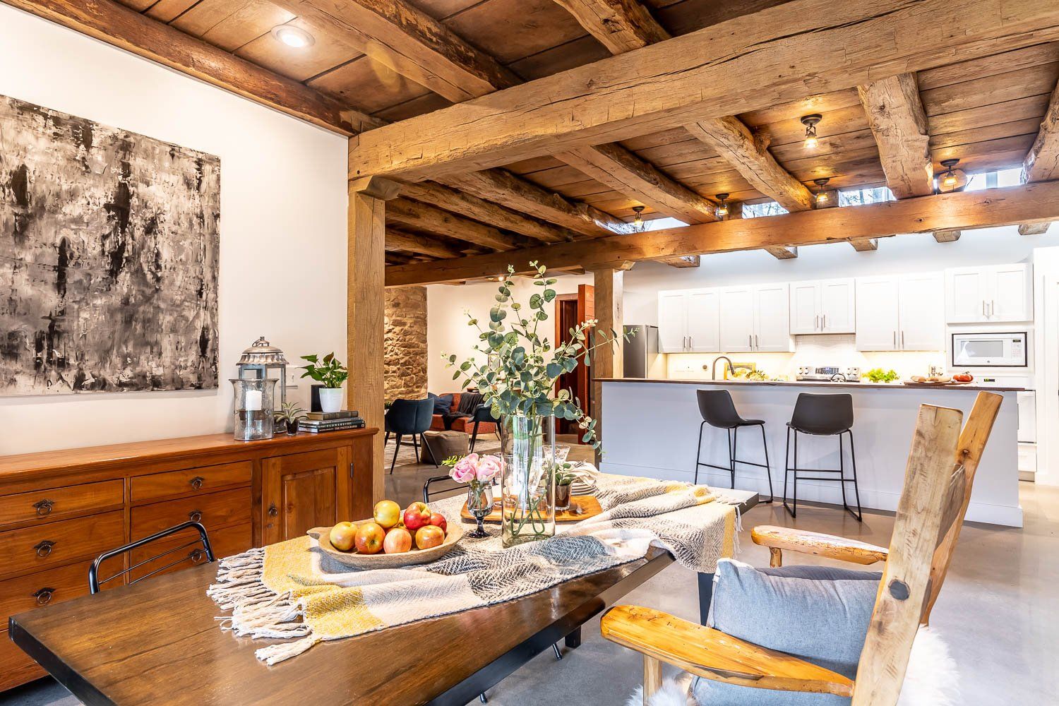 Dining room with wooden beams, a table set for a meal, and open kitchen.