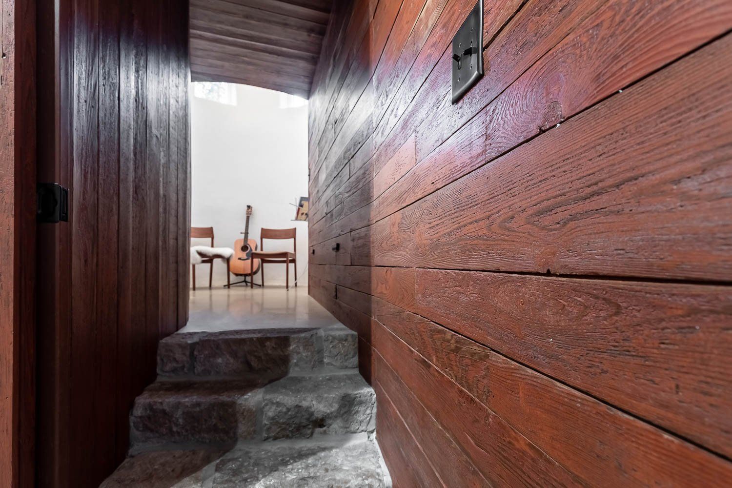 Stone steps lead up to a doorway; wood-paneled walls surround. A guitar and chairs sit in the adjacent room.