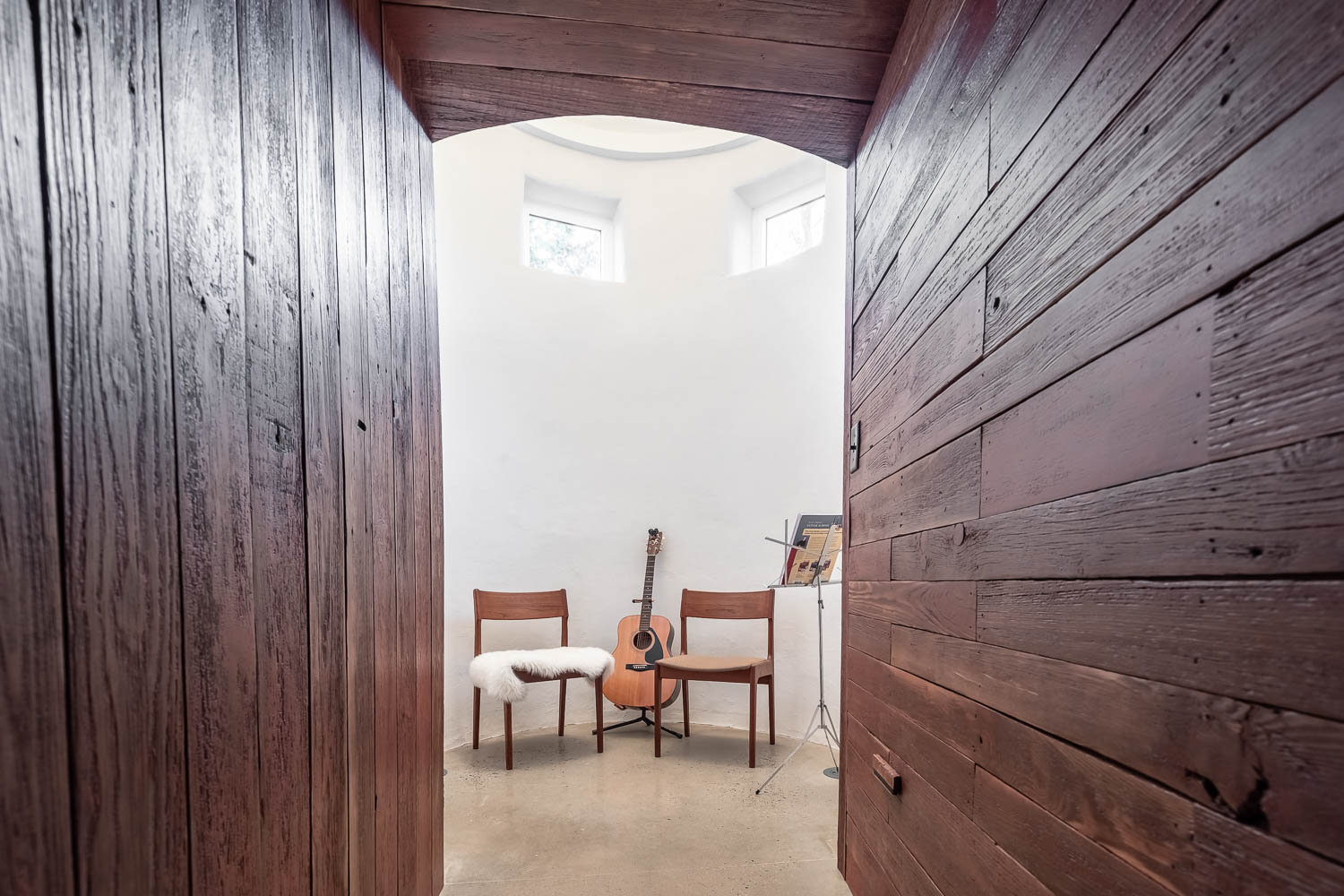 Wooden doorway leading into a white room with two chairs, a guitar, and round windows.