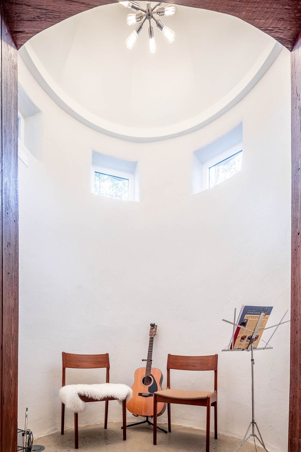 Acoustic guitar and music stand between chairs in a small, white, domed room with arched entrance.