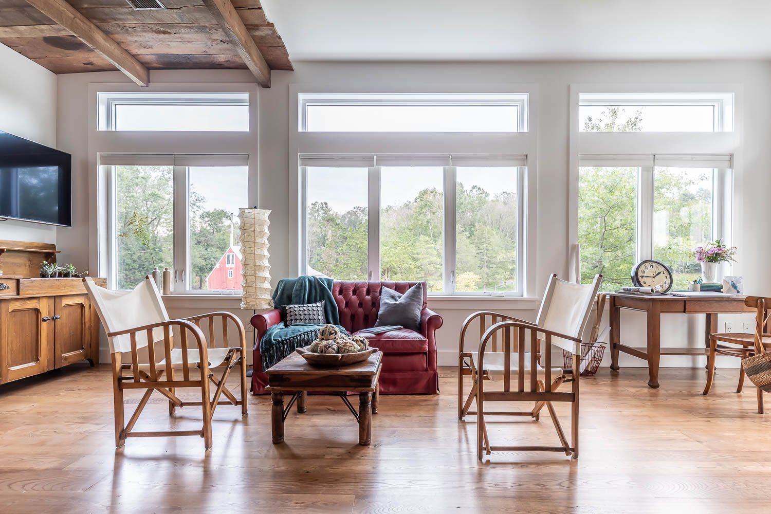 Living room with large windows, red couch, wooden chairs, and table.