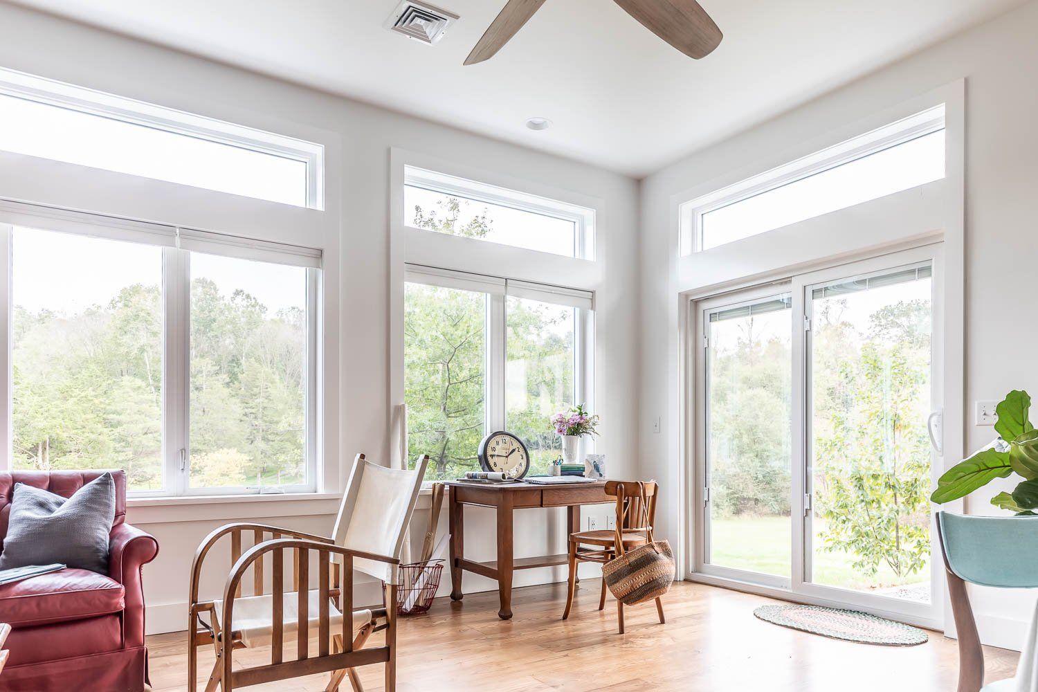 Bright living room with large windows, wooden furniture, and a view of greenery.