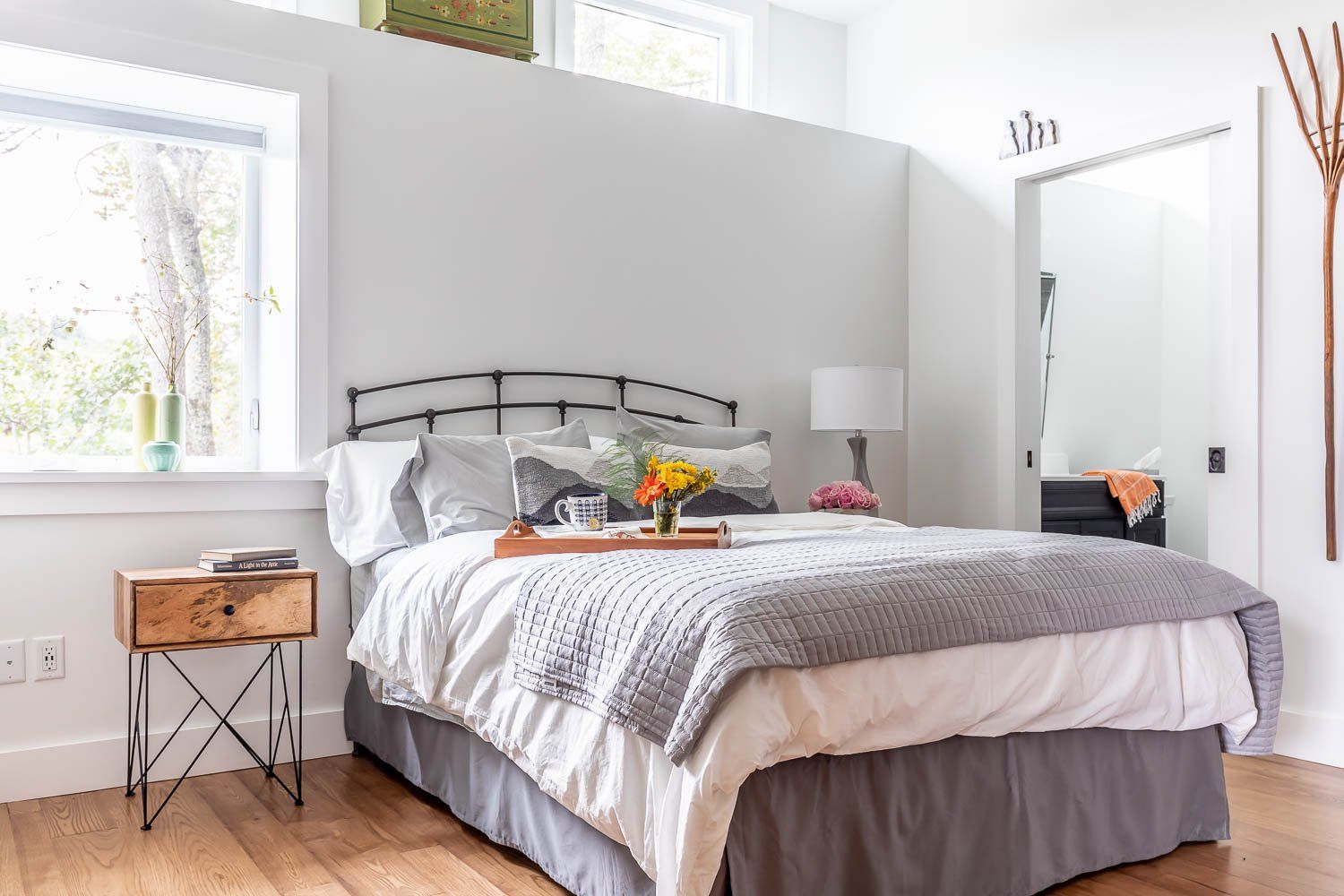 Bedroom with white walls, bed with gray bedding, wooden nightstand, and window.