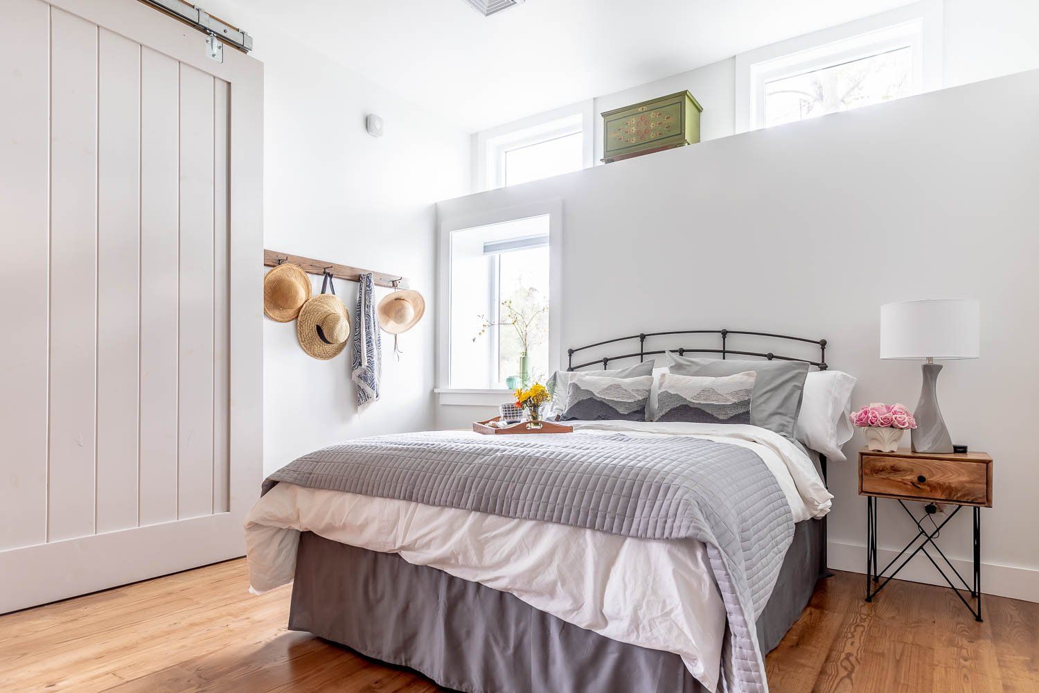 Bedroom with bed, nightstand, and hats on wall. Bright, white walls with natural light.