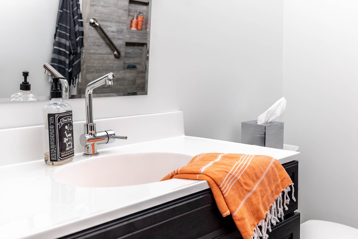 Bathroom vanity with a white countertop, oval sink, chrome faucet, orange towel, and tissue box.