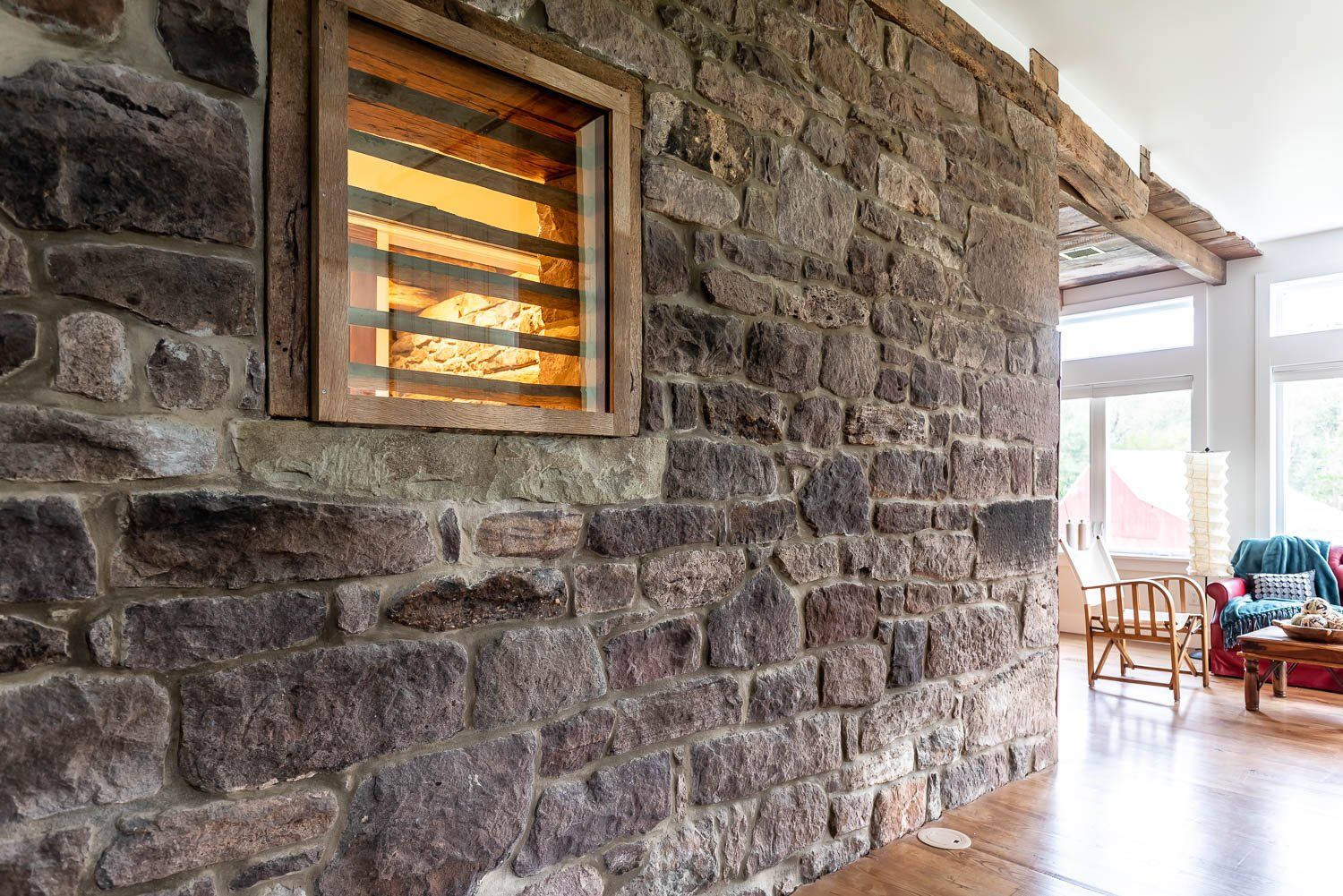 Stone wall with a wooden framed window and interior living space in the background.