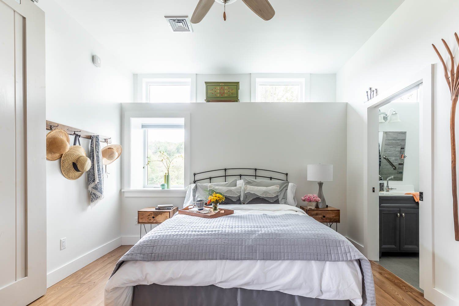 Bedroom with a bed, nightstands, and a small bathroom visible. White walls, wooden floor, neutral tones.
