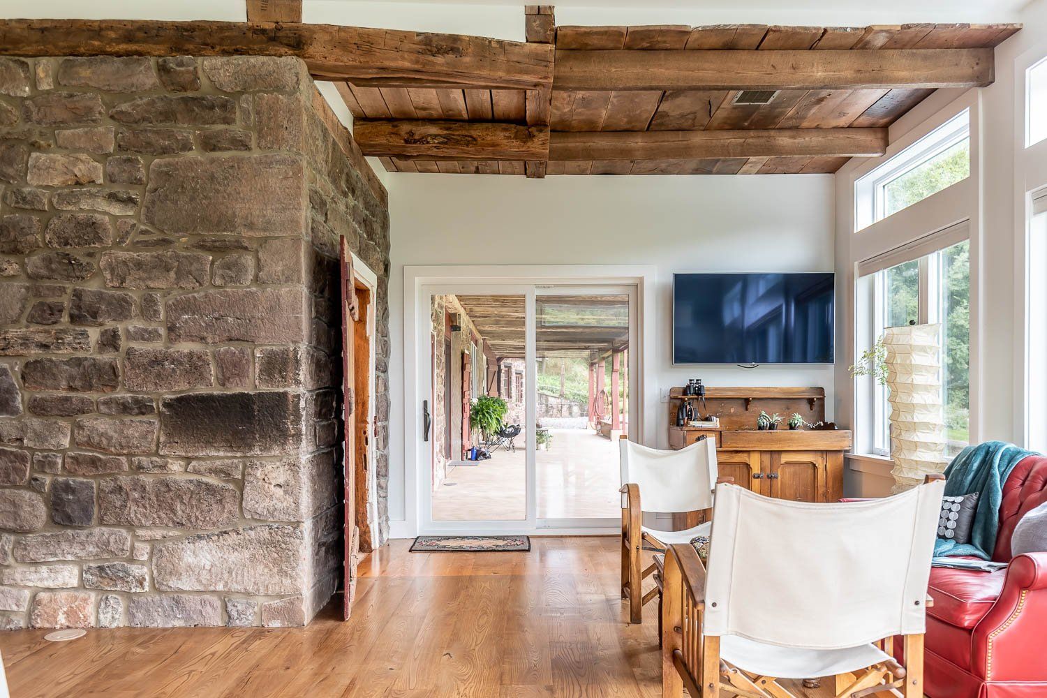 Interior with stone wall, wooden beams, hardwood floor, and sliding glass door to a porch.