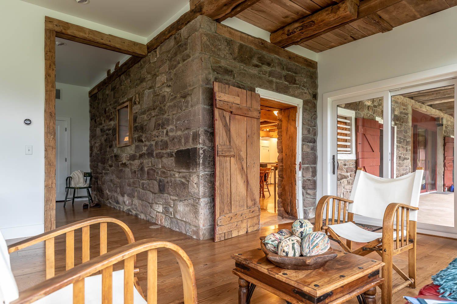 Sunroom with stone walls, wood shutters, chairs, and a small wooden table.