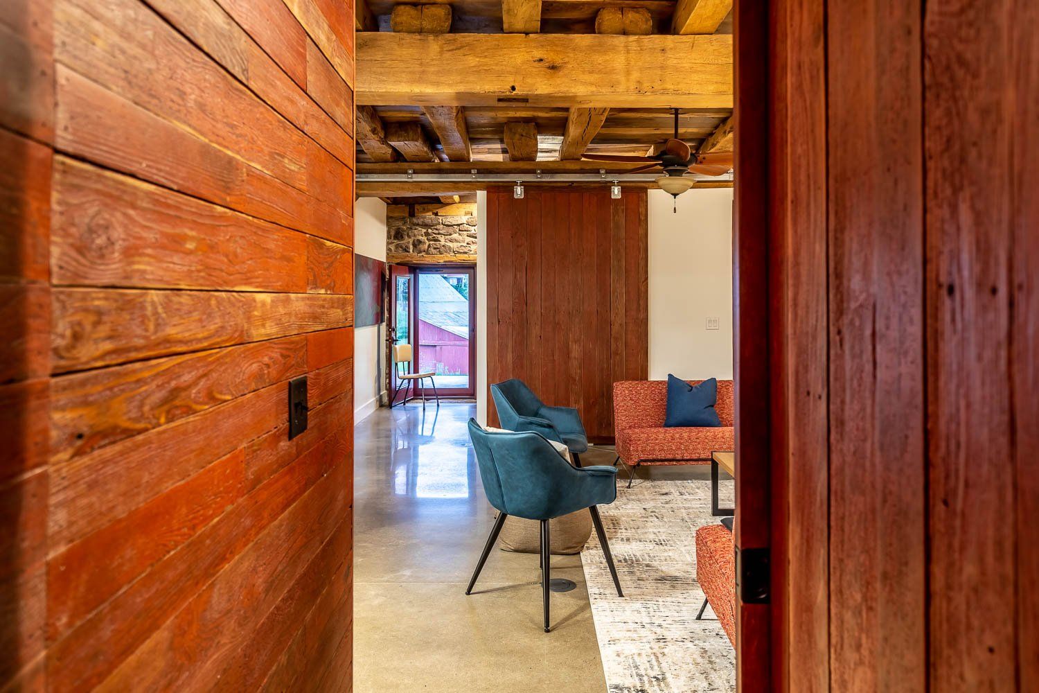 View through a wooden doorway into a living room with chairs, a couch, and exposed beams.