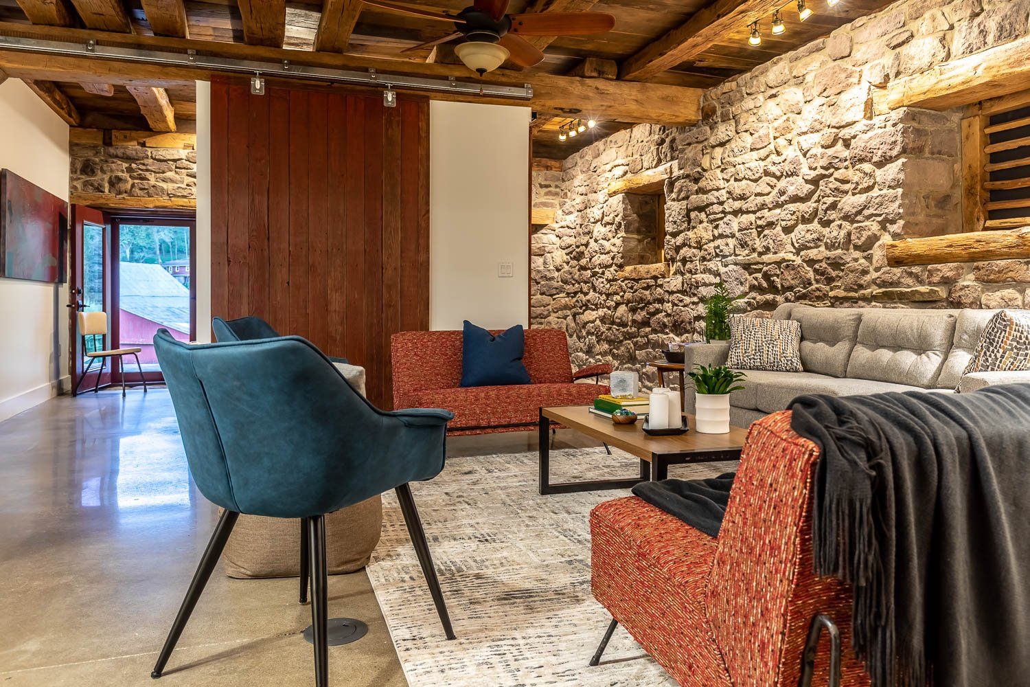 Living room with stone walls, wooden beams, seating, and a rug.