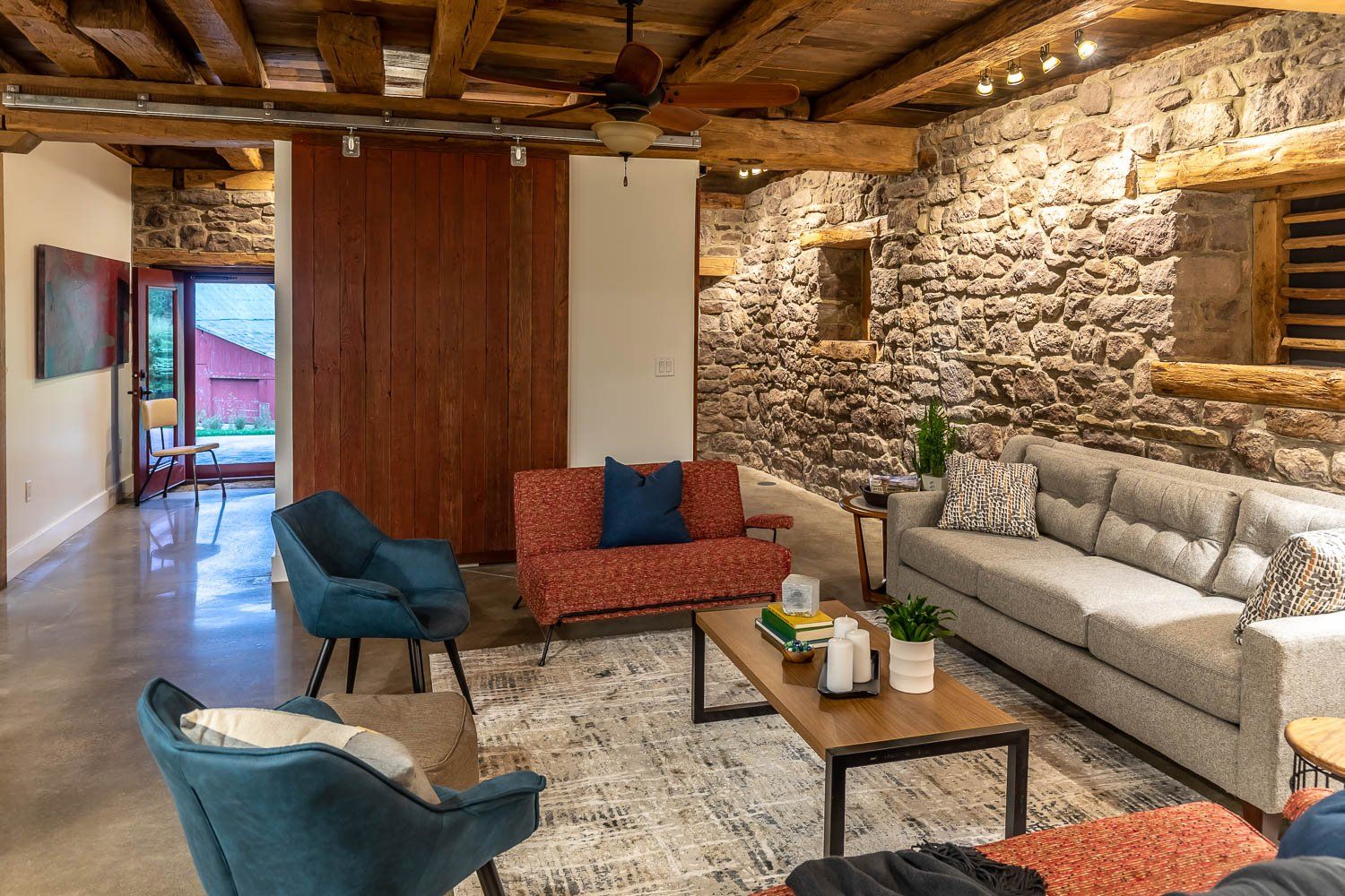 Living room with stone walls, wooden beams, various colored sofas, and a coffee table.