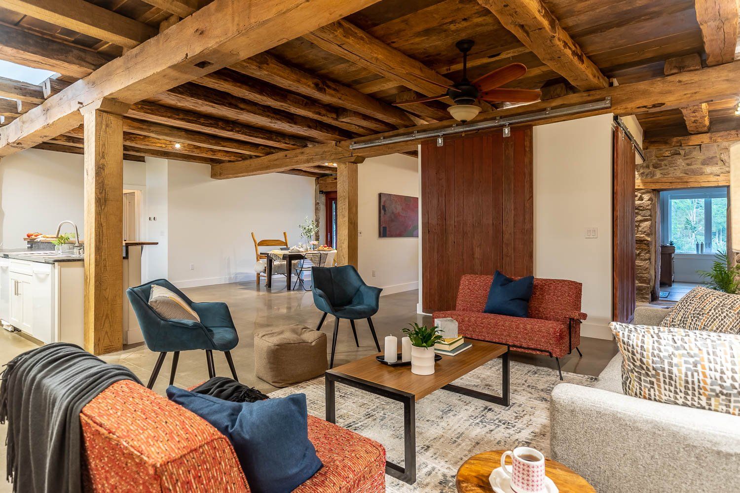 Living room with exposed wood beams, concrete floor, modern furniture, and a sliding wooden door.