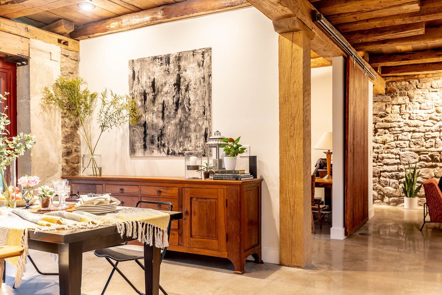 Rustic dining room with wooden beams, stone walls, and a buffet table.