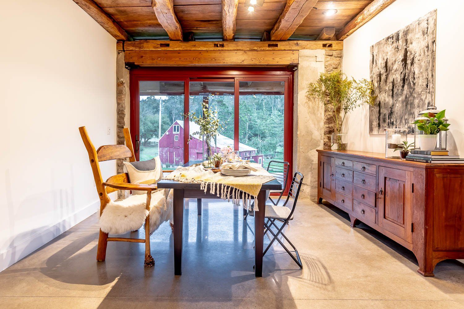 Dining room with wood beams, table set for meal, red framed sliding door to outside, and wood buffet.