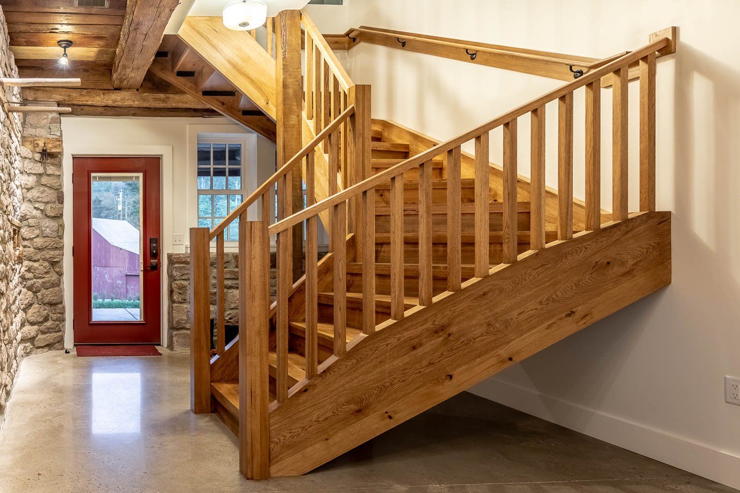 Wooden staircase in a home. The stairs have a railing on the side and a red door at the bottom.